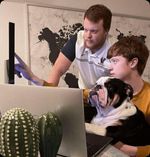 Collin and Will from Child Care Web Design collaborating at a computer with their mascot, illustrating dedication to custom websites for childcare centers.